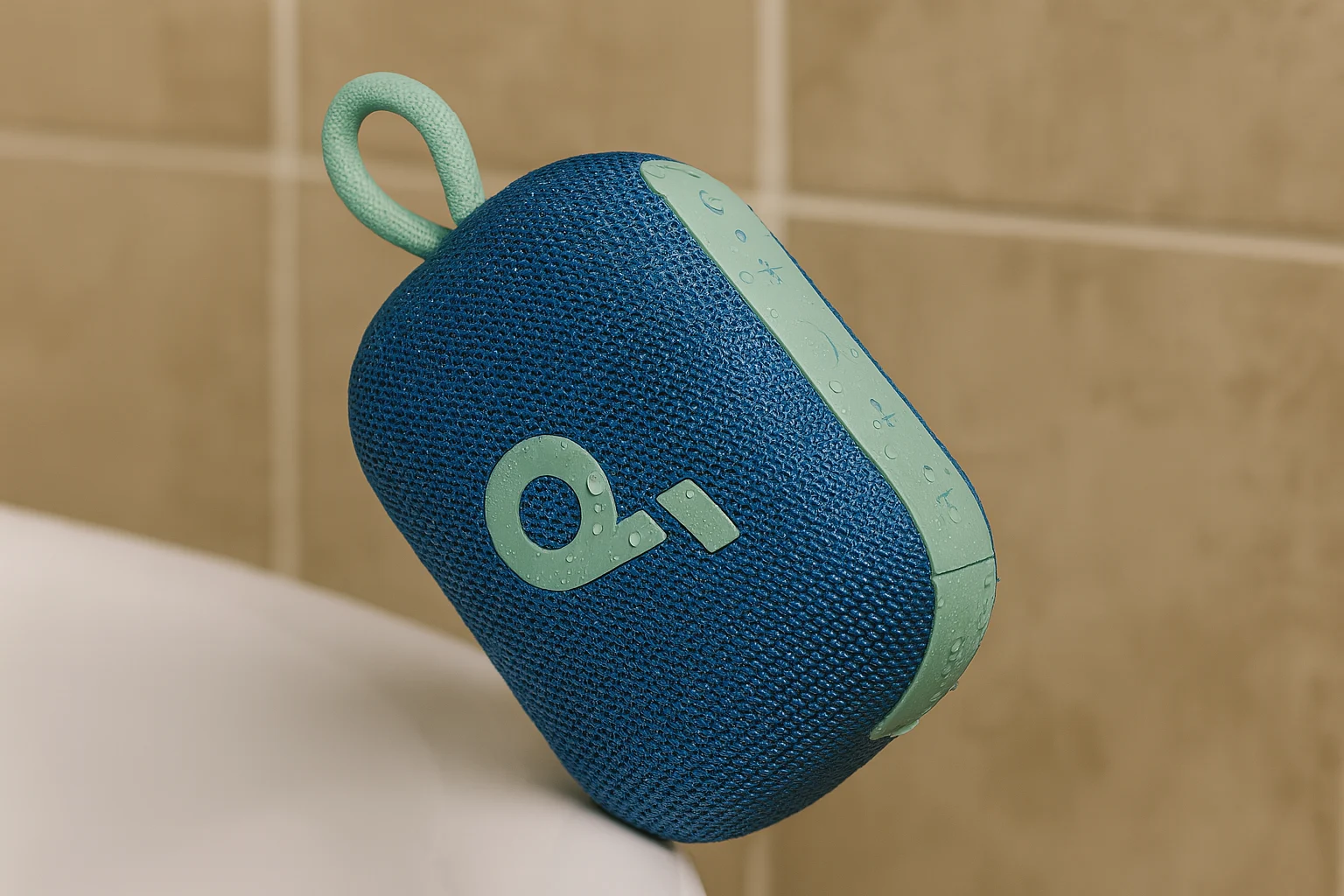 A waterproof Bluetooth shower speaker with a blue mesh body and mint green accents, placed on a bathroom surface with water droplets visible.