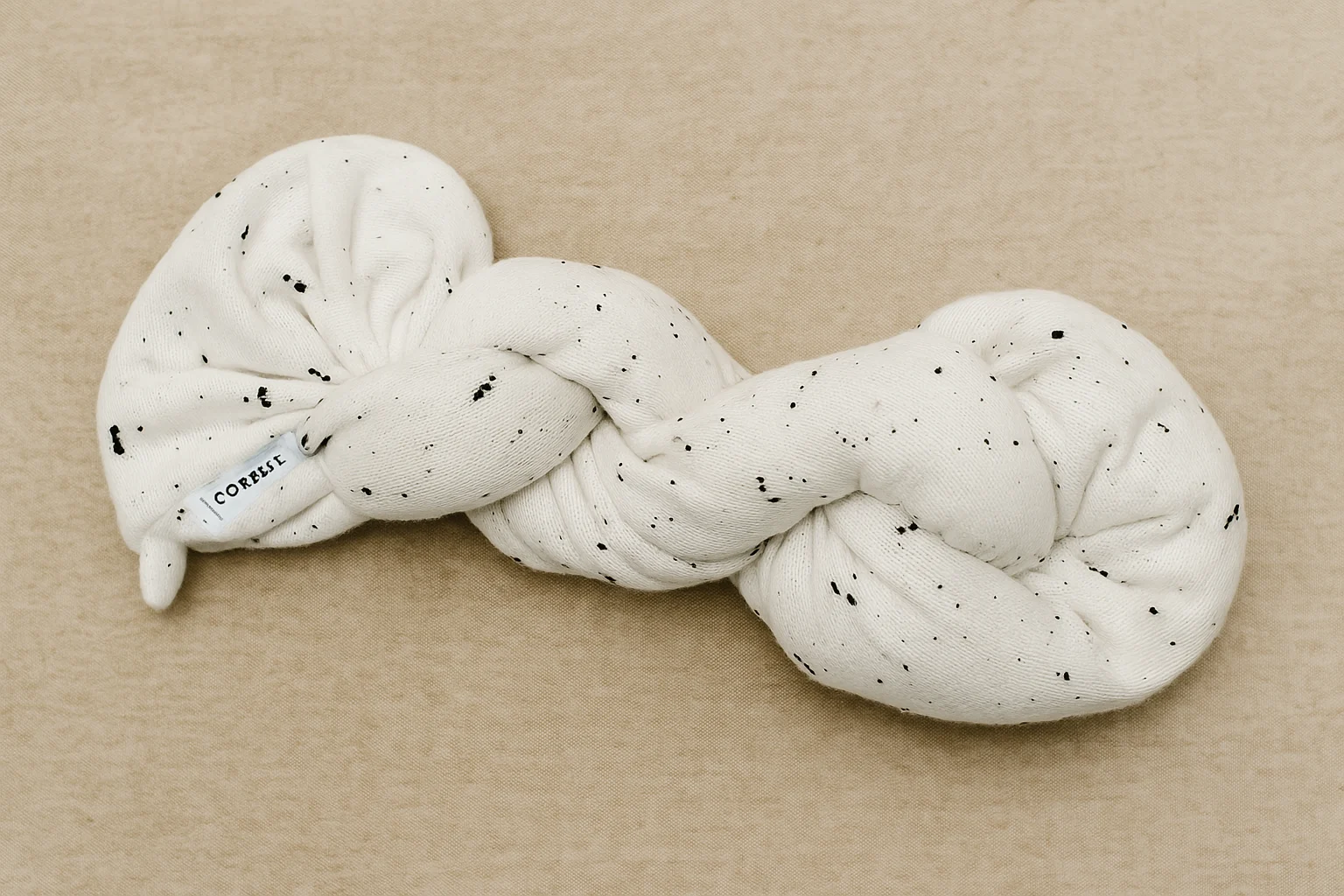Knotted eco-friendly baby product in soft white fabric with black specks, designed for safe lounging and modern nursery styling.